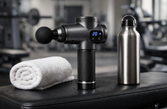 Hypervolt-style percussive massage gun on a gym bench with towel and water bottle