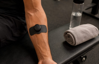 Wireless EMS muscle stimulator electrode pad on forearm at gym bench with towel and water bottle
