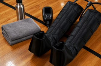 Pneumatic compression recovery boots on a wood gym floor next to a folded towel and stainless water bottle