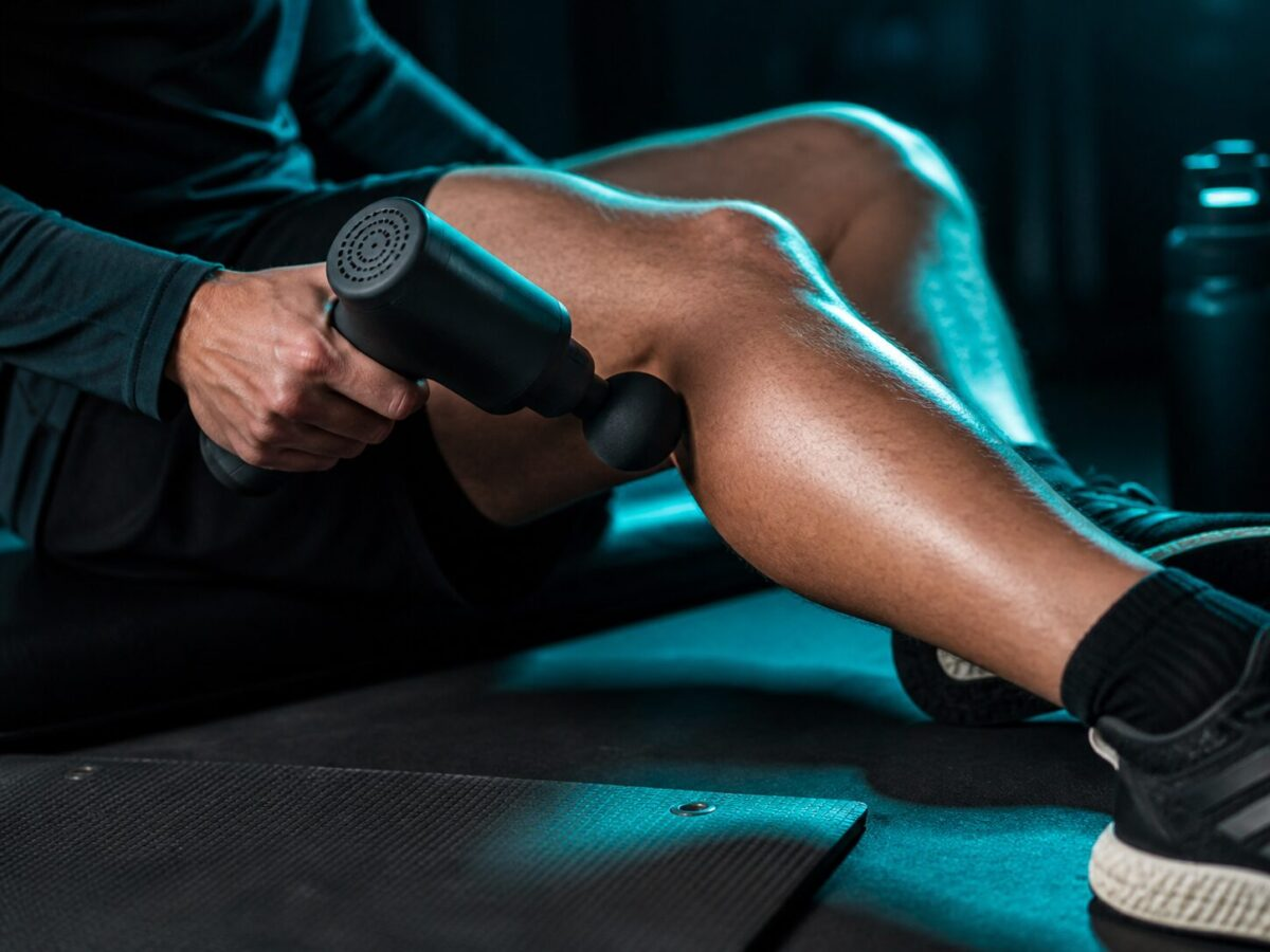Massage gun being used on a calf muscle in athletic recovery setting with dramatic teal accent lighting