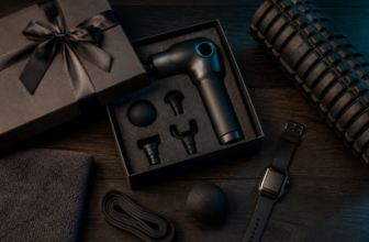 Father's Day gift box with massage gun, foam roller, smartwatch and recovery items on dark wood surface