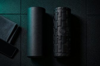 Two black foam rollers side by side on a dark gym floor, one with a power button
